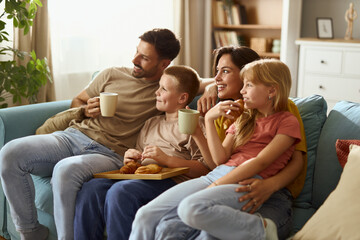 Happy parents and their kids day dreaming while relaxing on sofa at home.