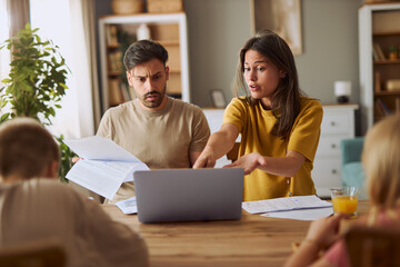 Frustrated parents talking about  financial bills during e-banking over a computer at home.