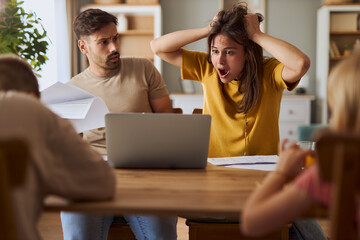 Frustrated parents talking about  financial bills during e-banking over a computer at home.