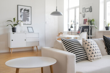 Obraz premium Modern Scandinavian living room with patterned cushions on white sofa and wooden furniture in bright interior