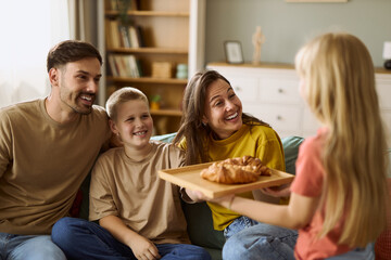 Happy  family enjoying in their time at home while daughter is bringing croissants to her parents...