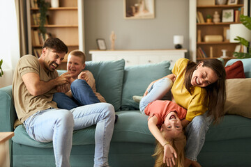 Cheerful parents having fun while tickling their small children at home.