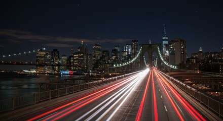 Obraz premium Long exposure shot of car light trails on a bridge leading to a city skyline at night.
