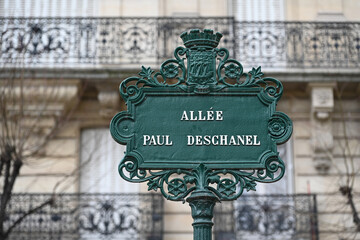 Paris, France : Elegant green Parisian street sign with ornate ironwork, historical architecture in the background. Allée Paul Deschanel, Paris