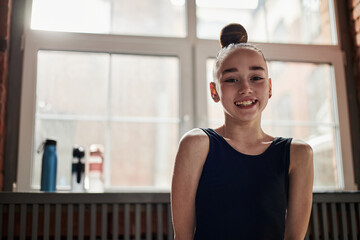 Portrait of Caucasian girl smiling at camera during rhythmic gymnastics training session in studio,...