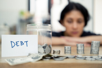 A woman sits at a table, looking distressed, with piled coins and a debt note. This scene expresses the concept of financial burden, economic challenges, and personal reflections on money management.