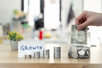 Person's hand depositing money into a savings jar, with coins stacked nearby and a note signifying growth, embodying themes of financial planning, success, and investing for the future.
