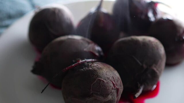 The boiled beet is cooling on the kitchen table.
A burgundy beet with unpeeled skin lies on a white plate.
Healthy vegetables and proper nutrition
