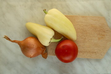 Fresh vegetables including tomato, peppers, and onion on a wooden cutting board. 