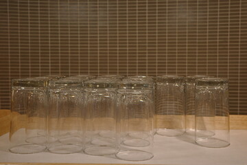 Neatly arranged row of clear drinking glasses turned upside down on a white surface with a tiled...