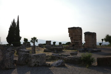 Broken stone structures and scattered ruins in soft evening light, with silhouetted trees in the...