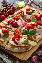 Pinsa Romana with boiled ham, burrata cheese, basil leaves and cherry tomatoes on wooden table	
