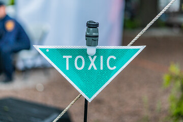 Close-up of a diamond-shaped TOXIC sign on a black wire fence, in a natural green environment with...