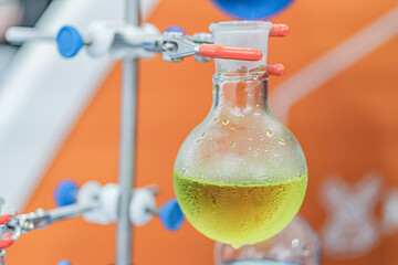 Close-up view of a scientific setup, featuring an Erlenmeyer flask bubbling green liquid, connected...