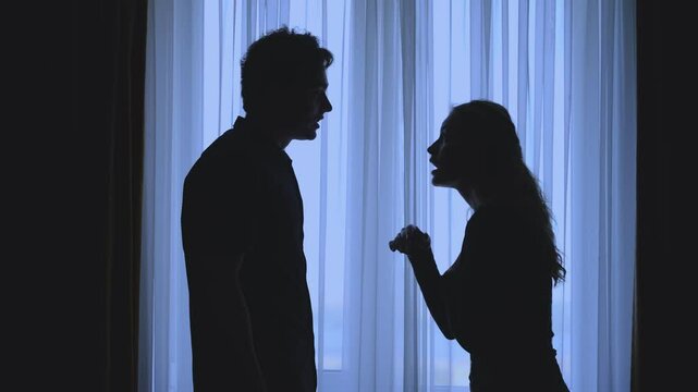 couple quarreling concept of family relationship problems divorce, black silhouette of man and woman shouting at each other at window in dark room. Guy shaking cry girl causing ol cruel hurting abuse