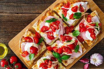 Pinsa Romana with boiled ham, burrata cheese, basil leaves and cherry tomatoes on wooden table	