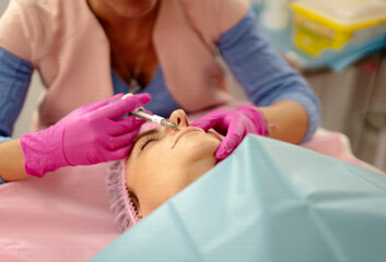 Beautician injecting filler into woman's nose for rhinoplasty treatment