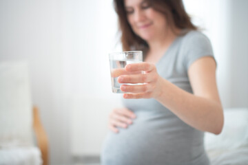 Close-up of pregnant woman drinking water, focusing on self-care and prenatal health. Cozy home...