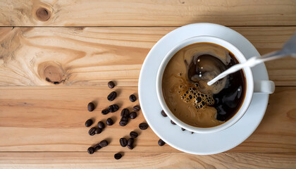 Cup of coffee with milk being poured into it sits on wooden table, surrounded by scattered coffee beans. overhead view captures swirling motion of milk blending with coffee