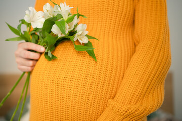 Expecting mother cradling white flowers while lovingly touching her baby bump. Pregnant woman