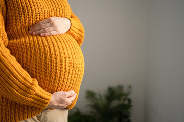 Serene close-up of pregnant woman's hands lovingly touching her baby bump. Heartwarming scene of prenatal connection in cozy home environment.