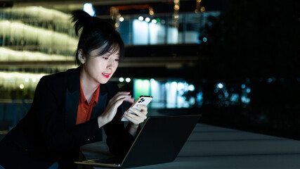 Woman using smartphone and laptop outdoors at night