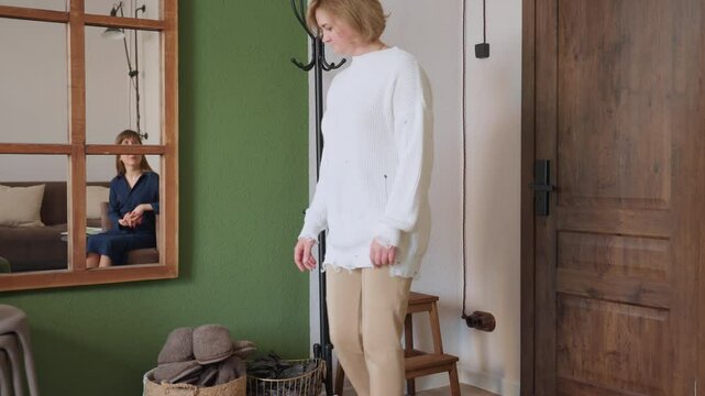Patient wears brown crocs by side of room near door, basket and coat rack in view, while mirror on green wall reflects therapist seated on sofa calmly waiting, creating professional atmosphere