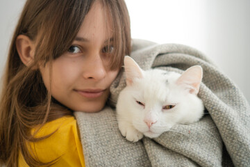 Adolescent female holding her pristine white cat in loving embrace. Beautiful demonstration of pet friendship and devotion.