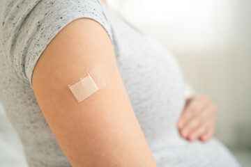 Close-up of expecting mother with bandage on forearm post-immunization. Thoughtful moment of prenatal healthcare and maternal protection.