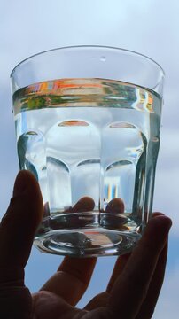 Drinking water in the hands of a man against the sky in hot weather.
A glass of refreshing and cool water in a glass cup.
A man drinks water to feel better