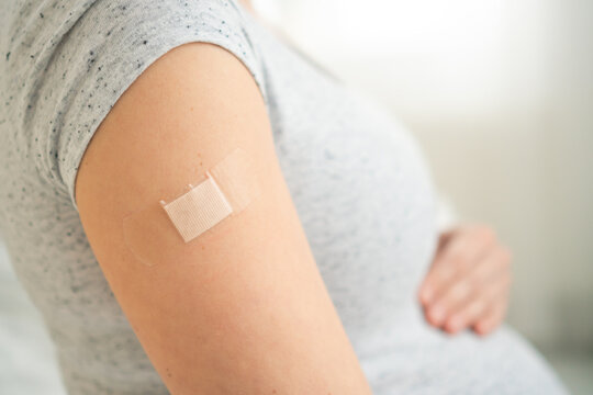Close-up of expecting mother with bandage on forearm post-immunization. Thoughtful moment of prenatal healthcare and maternal protection.