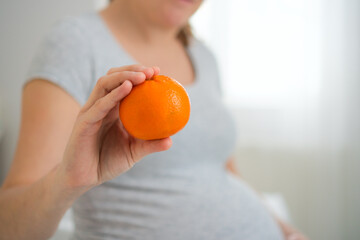 Close-up of pregnant woman holding orange while lovingly stroking her rounded belly. Nourishing citrus snack during precious pregnancy connection time.