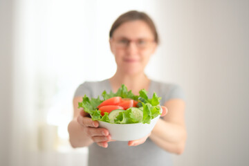 Close-up of pregnant woman holding nutritious vegetable salad while stroking her baby bump. Balanced diet moment of maternal care and wellbeing.