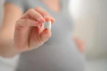 Future mother's hand holding essential pregnancy vitamin near her belly. Important nutritional supplement for maternal and fetal health.