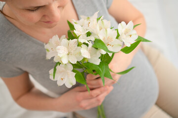 Serene close-up of pregnant woman's hands with white blooms gently resting on rounded abdomen. Heartwarming prenatal bonding scene.