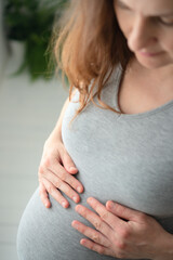Close-up of expecting mother gently stroking her rounded belly in peaceful home setting. Tender moment of maternal connection and anticipation.