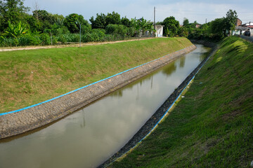 Water Management Canal with Stone Lined Banks and Green Grass Under Sunny Sky