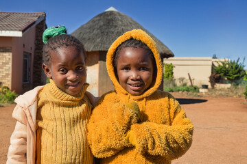African village, two child girl with braids , standing in front of the house, wearing yellow...