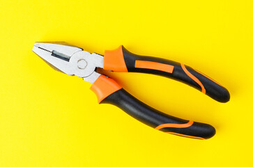 Metal pliers tool with rubber handles on bright yellow background top view