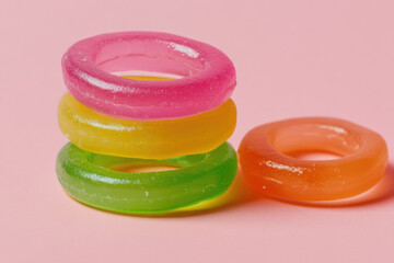 Bright neon-colored jelly candy rings, piled together on a soft neutral background, creating an eye-catching display. 