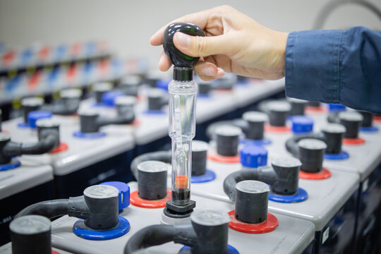 Technician inspects backup battery power system using hydrometer to ensure optimal performance and safety in industrial environment with multiple connected batteries