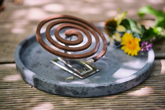 Burning mosquito coil with citronella on a wooden table outdoors in summer. Eye level view. Lifestyle concept.