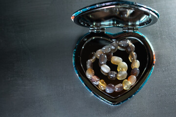 An earthy agate bead bracelet coiled within a heart-shaped mirrored box, symbolizing self-love,...