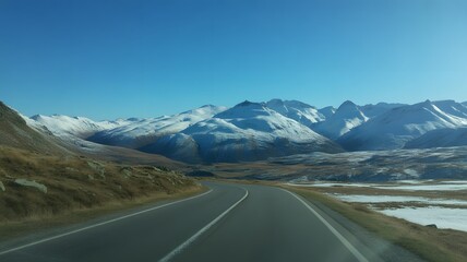 Scenic road winding through majestic snow capped mountain peaks under bright blue sky