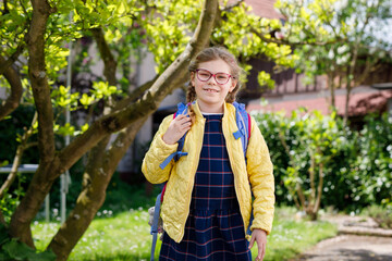 Happy little kid girl with eye glasses with backpack or satchel and big school bag on the first day...