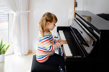 Beautiful little toddler girl playing piano in living room. Cute preschool child having fun with...