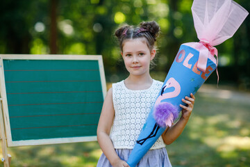 Happy little kid girl by desk with backpack or satchel and big school bag or cone traditional in...