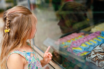 Happy preschool girl choosing and buying ice cream in outdoor stand cafe. Cute child looking at...