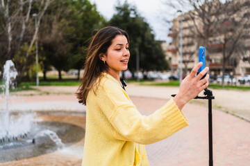 Young woman vlogging in a city park, using a smartphone on a gimbal to create engaging content for her followers