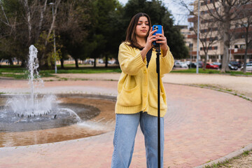 Young woman recording video content in a park using a smartphone and tripod, near a fountain